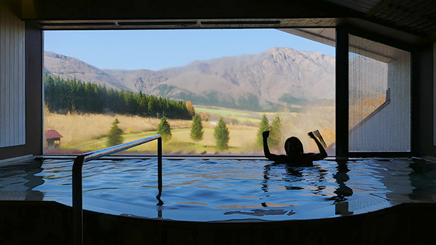 青空と山が見えるホテルオニコウベの温泉につかり、ガッツポーズする筆者