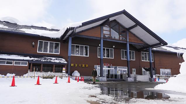 木造風の外観の新玉川温泉の施設の入り口に立つ筆者