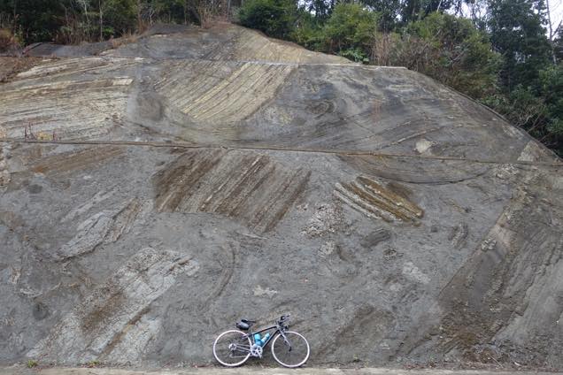 海底の地すべりの後がギザギザに残る大きな岩にロードバイクを立てかける