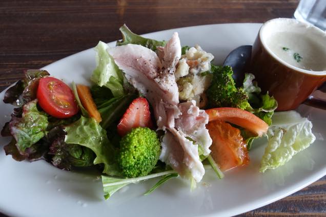 トマト、レタス、ブロッコリー、イチゴ、ポテトサラダ、ハムが盛られたサラダとポタージュ