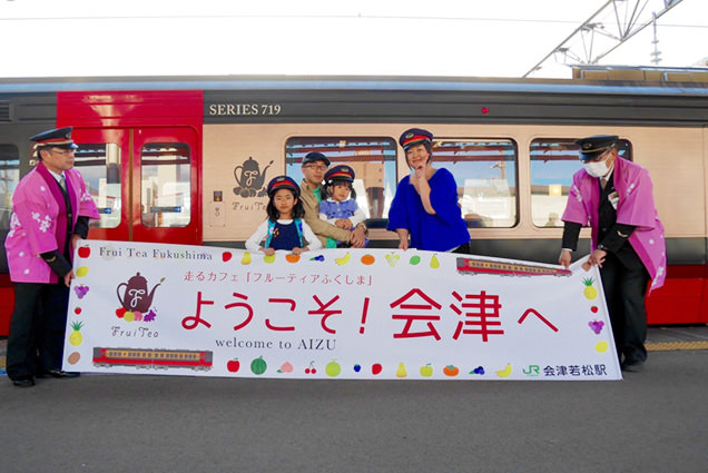フルーティアふくしまの列車の前で、駅員さんの帽子をかぶり記念撮影をする家族